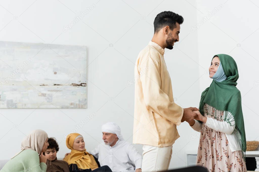 smiling interracial father and daughter holding hands near muslim family at home