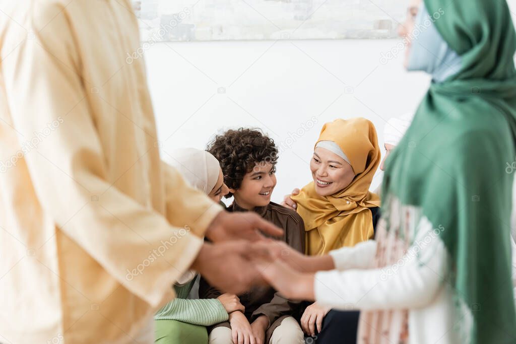 blurred man holding hands of daughter near happy multiethnic muslim family