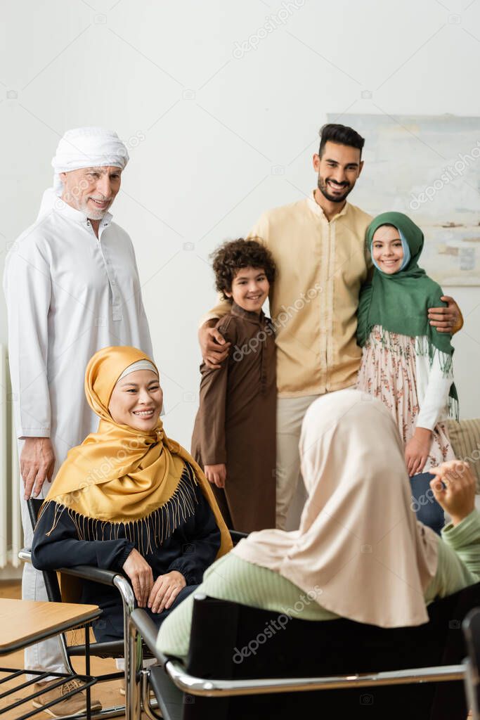 smiling arabian man embracing kids near multiethnic muslim family talking at home