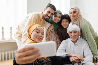 Tesettürlü Asyalı kadın cep telefonuyla çok ırklı Müslüman ailesiyle selfie çekiyor.