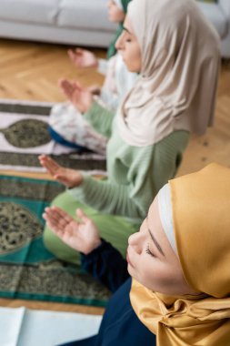 Yüksek açılı, gözleri kapalı Müslüman bir kadının evinde kızının ve torununun yanında dua edişinin görüntüsü.