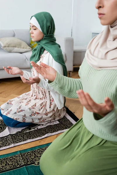 閉じられた目をしたイスラム教徒の少女は自宅の敷物の上でアラビア語の母の近くで祈ります — ストック写真