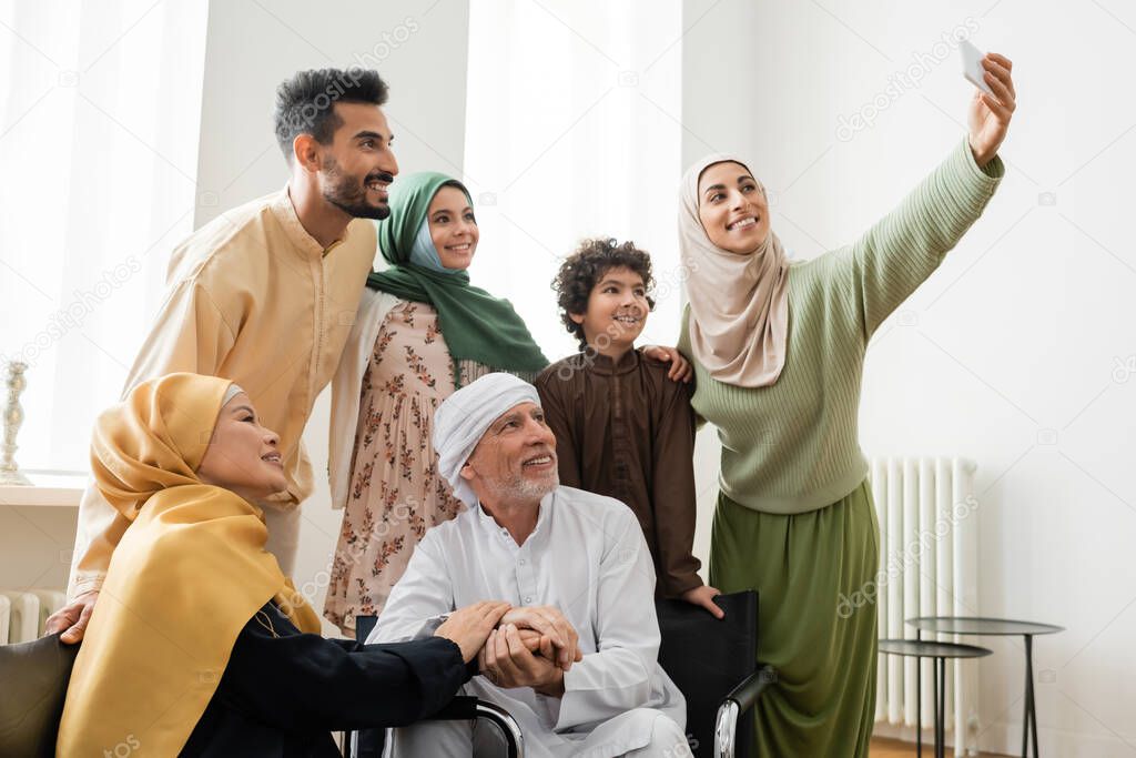 happy arabian woman taking selfie on smartphone with multicultural muslim family