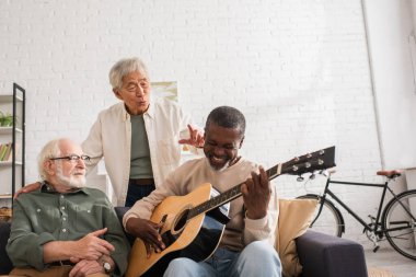 Memlekette çok ırklı arkadaşların yanında akustik gitar çalan neşeli Afrikalı Amerikalı adam. 
