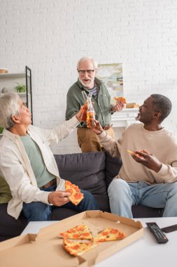Çok kültürlü son sınıf arkadaşları biralarını lezzetli pizzanın yanında tokuşturuyorlar ve evde uzaktan kumanda var. 