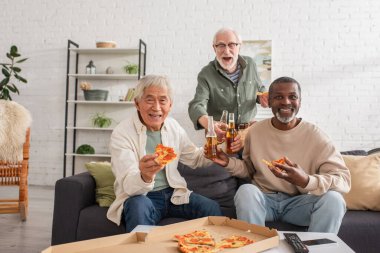Evde pizza ve bira şişeleri tutan mutlu yaşlı insanlar. 