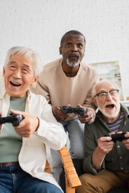 KYIV, UKRAINE - 12 Ekim 2021: Evde video oyunu oynayan yaşlı çok ırklı yaşlılar 