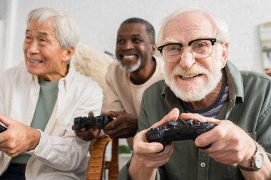 KYIV, UKRAINE - 12 Ekim 2021: Memlekette bulanık etnik gruplar içinde video oyunu oynayan odaklanmış yaşlı adam 