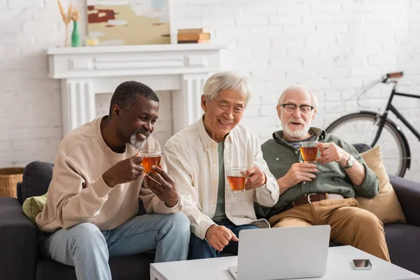 Smiling Interracial Friends Using Laptop Holding Tea Home — Stock Photo, Image