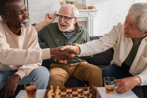 Smiling Senior Man Holding Tea Interracial Friends Shaking Hands Chess — Stock Photo, Image