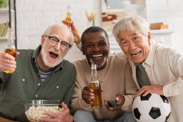 Smiling Interracial Senior Friends Beer Popcorn Remote Controller Looking Camera — Foto de Stock