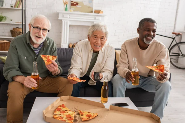 Evde televizyon izlerken pizza ve bira içen pozitif ırklar arası kıdemli arkadaşlar. 