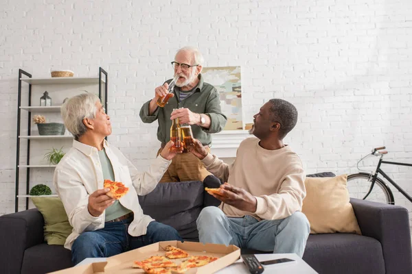 Ancianos Amigos Multiétnicos Tintineo Cerveza Cerca Pizza Mando Distancia Casa — Foto de Stock
