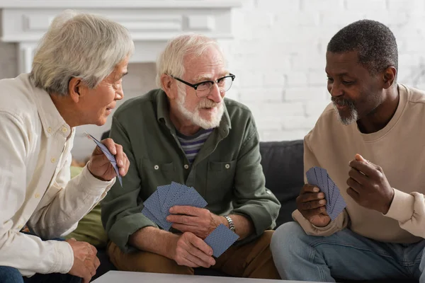 Positive Pensjonister Med Flere Raser Som Spiller Kort Hjemme – stockfoto