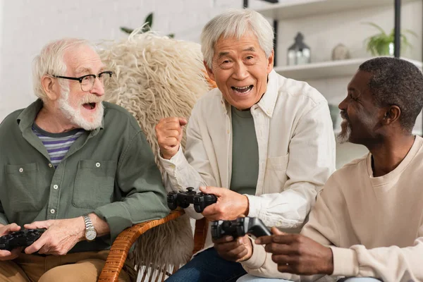 2021年10月12日 兴奋的亚裔男子在家中与多种族朋友玩电子游戏时表现出肯定的姿态 — 图库照片
