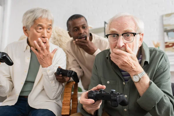 2021年10月12日 震惊的老年人在家里和模糊的多文化朋友玩电子游戏 — 图库照片