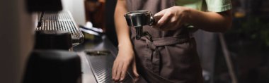 Cafe 'de kahve makinesinin yanında portafilter tutan baristanın kırpılmış görüntüsü. 