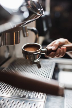 Kahve makinesinin önünde kahve makinesinin yanında portafilter tutan baristanın görüntüsü kesilmiş. 