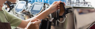 Cropped view of barista holding jug near steam wand of coffee machine in cafeteria, banner  clipart