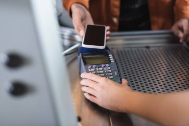 Kafe 'de cep telefonu olan Afrikalı Amerikalı bir müşterinin ödeme terminalini elinde tutan baristanın görüntüsü kesilmiş. 