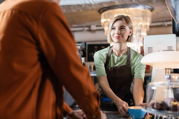 Barista Sonriente Delantal Sosteniendo Café Para Cerca Borrosa Cliente Afroamericano — Foto de Stock