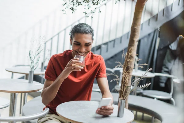 Hombre Afroamericano Feliz Usando Teléfono Inteligente Sosteniendo Vaso Café Cafetería — Foto de Stock