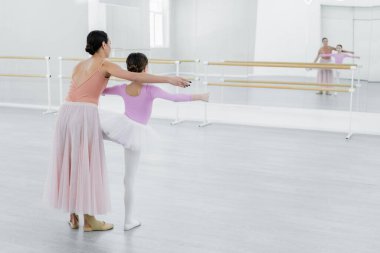 back view of girl training in ballet school near mirrors and young dance teacher clipart