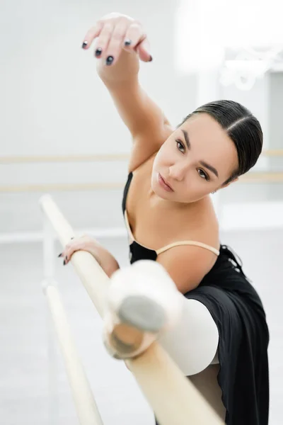 graceful woman stretching on barre in ballet studio