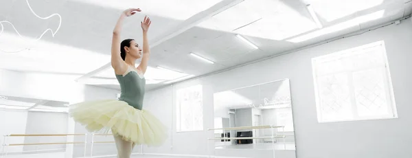 young ballet dancer with raised hands rehearsing in dancing hall, banner