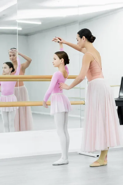ballet teacher raising hand of girl learning to dance ballet in studio