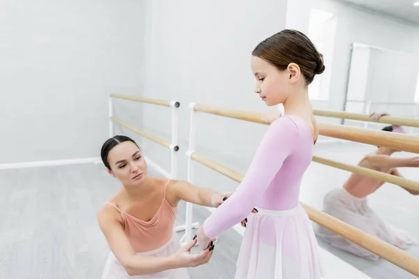 young ballet teacher assisting preteen girl in dance school