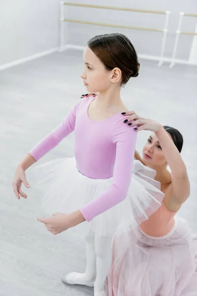 ballet teacher touching shoulders of girl during rehearsal in studio