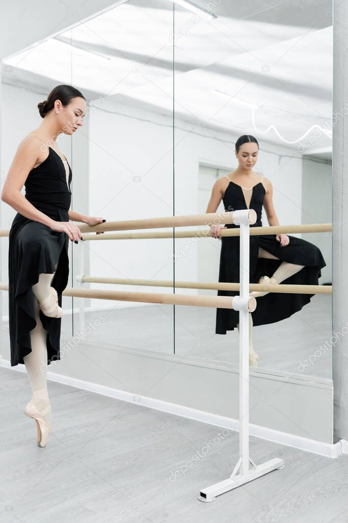 ballerina in black dress practicing choreographic elements in studio