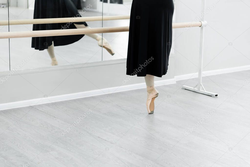 partial view of ballet dancer practicing at barre near mirrors