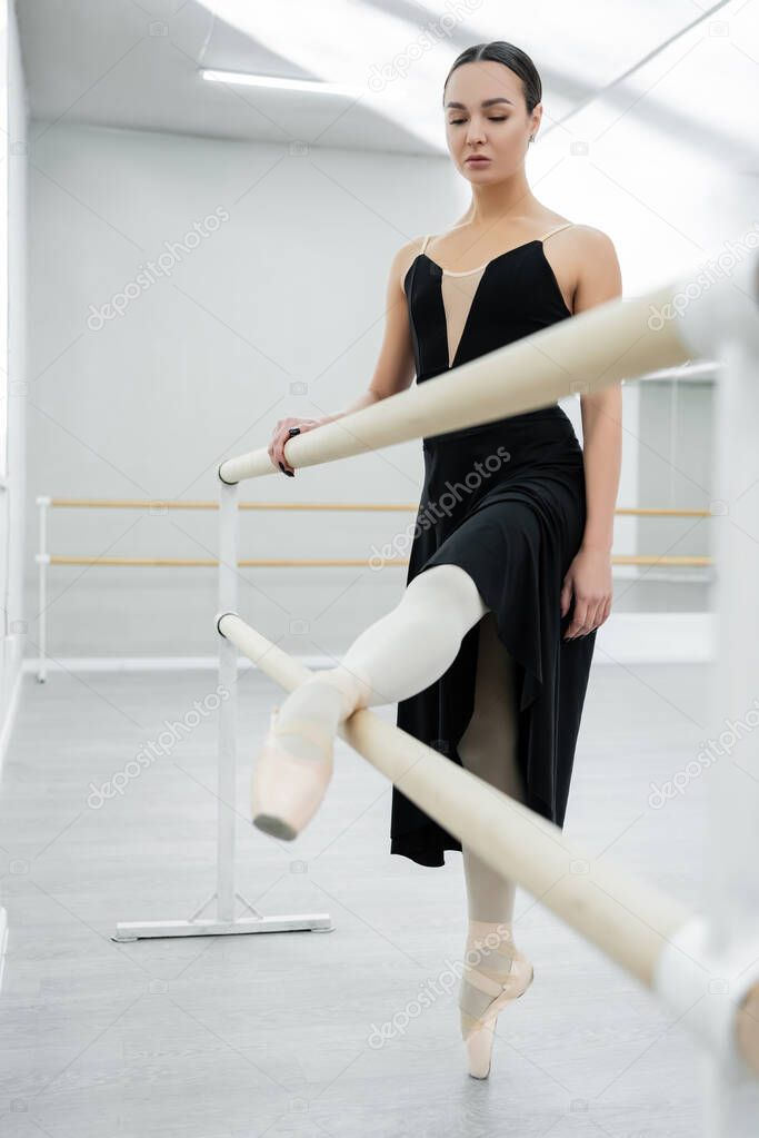 ballerina in black dress stretching at barre in dancing hall