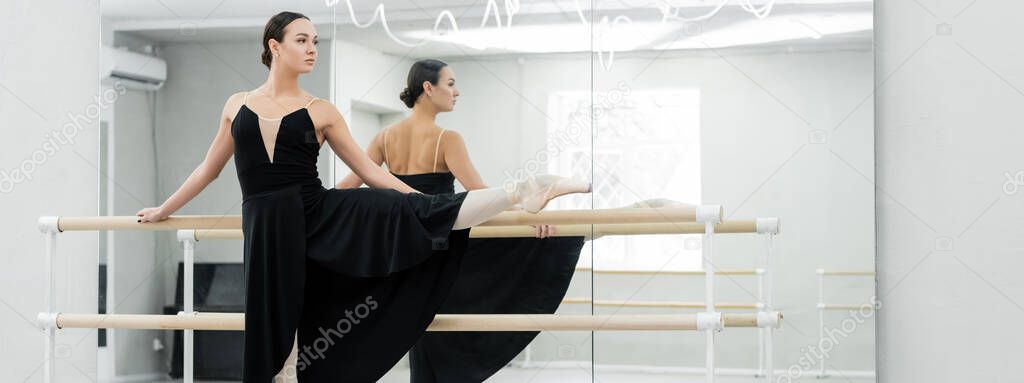 young ballerina in black dress rehearsing near mirrors in studio, banner