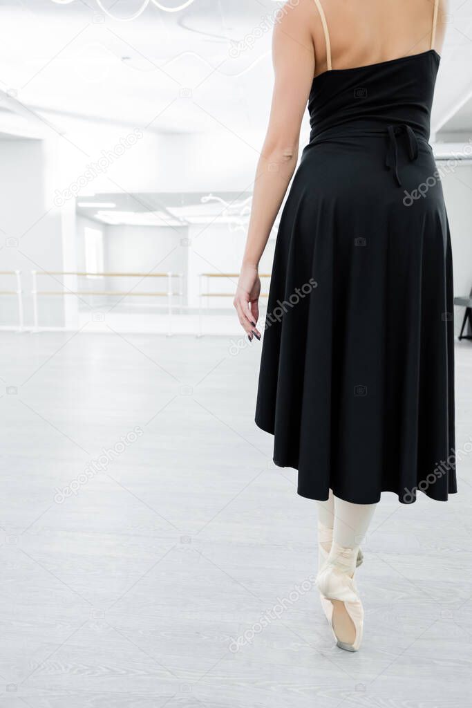 back view of cropped ballerina in black dress rehearsing in studio