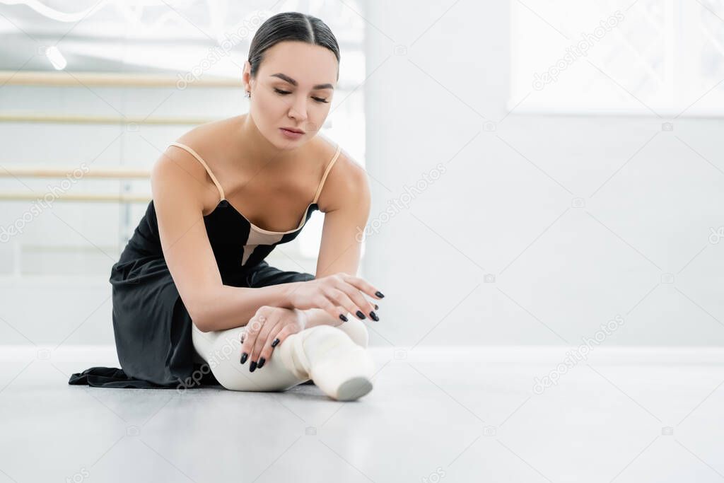 brunette ballerina stretching while sitting on floor in studio