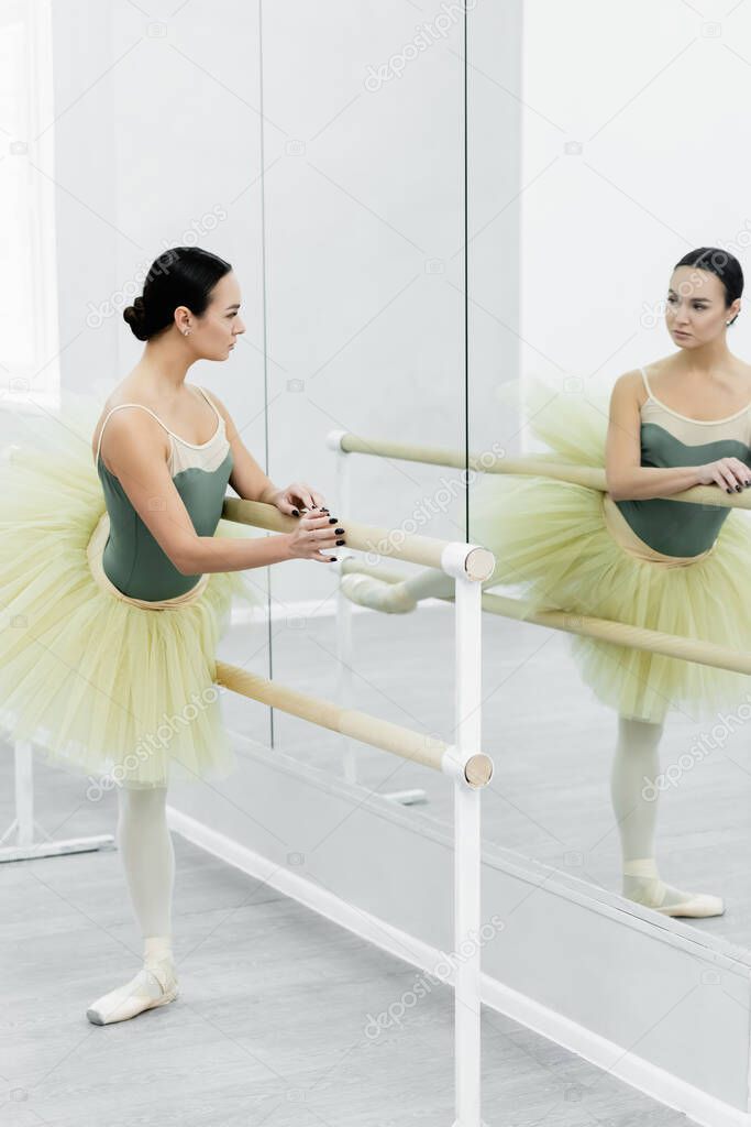 young ballerina looking in mirror while stretching at barre 