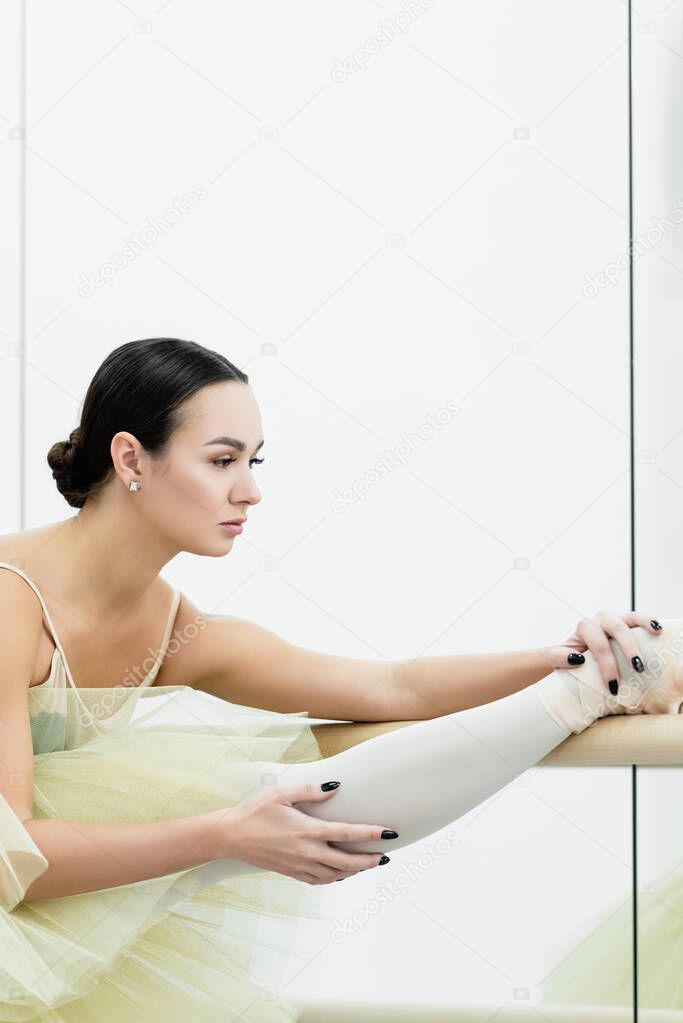 Young ballerina stretching leg at barre in dance studio