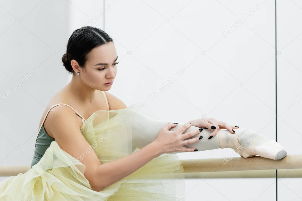 young ballerina stretching leg while training in dancing hall