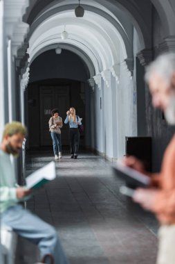 Kahve ve dizüstü bilgisayarlı ırklar arası öğrenciler üniversite koridorunda yürüyor. 