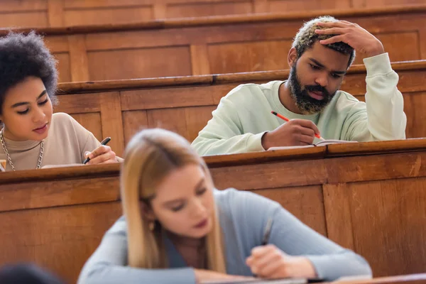 美国黑人学生在大学礼堂的朋友旁边的笔记本上写字 — 图库照片