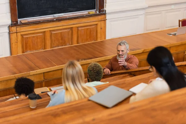 Positive teacher talking to interracial students in auditory of university