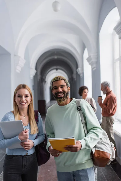 Uśmiechnięci Wielonarodowi Studenci Notatnikami Laptopem Patrzący Kamerę Korytarzu Uniwersyteckim — Zdjęcie stockowe