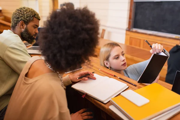 Estudiante Escribiendo Cuaderno Cerca Amigos Afroamericanos Auditorio Universitario — Foto de Stock