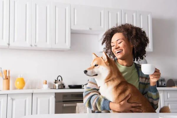 Riéndose Africana Americana Mujer Sentado Cocina Con Taza Café Shiba — Foto de Stock