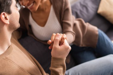 Evdeki kanepede bulanık Afrikalı Amerikalı kız arkadaşının elini tutan adam. 