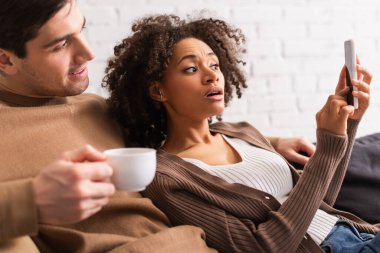 Evinde bulanık bardakla akıllı telefonları işaret eden Afrikalı Amerikalı bir kadın. 