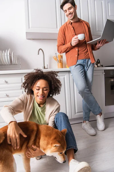快乐的非洲裔美国女人在厨房里用笔记本电脑和咖啡爱抚男友 — 图库照片